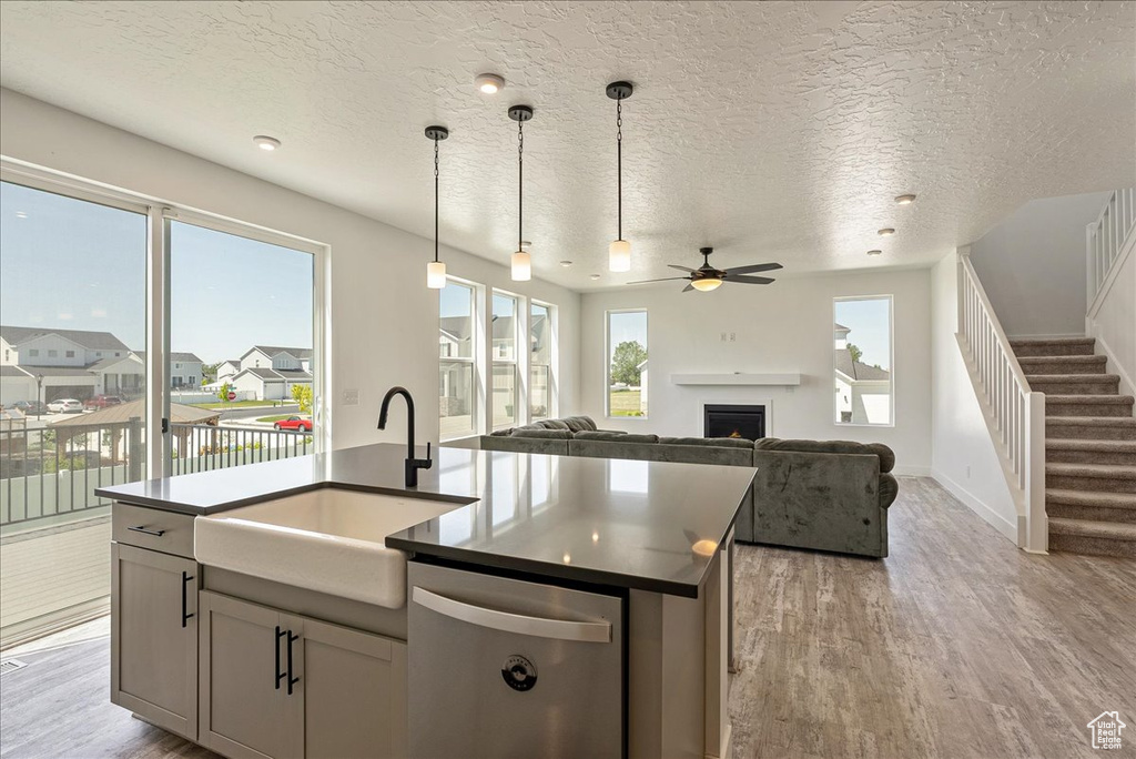 Kitchen with stainless steel dishwasher, a sink, light wood-style floors, dark countertops, and a textured ceiling