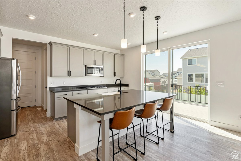 Kitchen with appliances with stainless steel finishes, dark countertops, gray cabinetry, light wood-style floors, and a breakfast bar