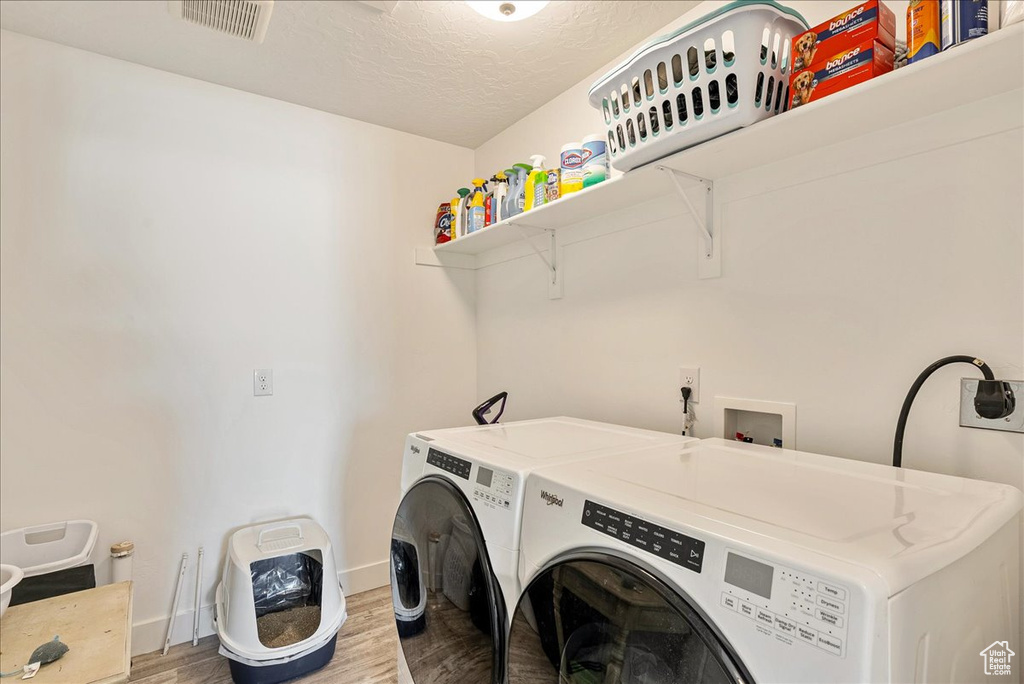Laundry room with wood finished floors, separate washer and dryer, baseboards, and a textured ceiling