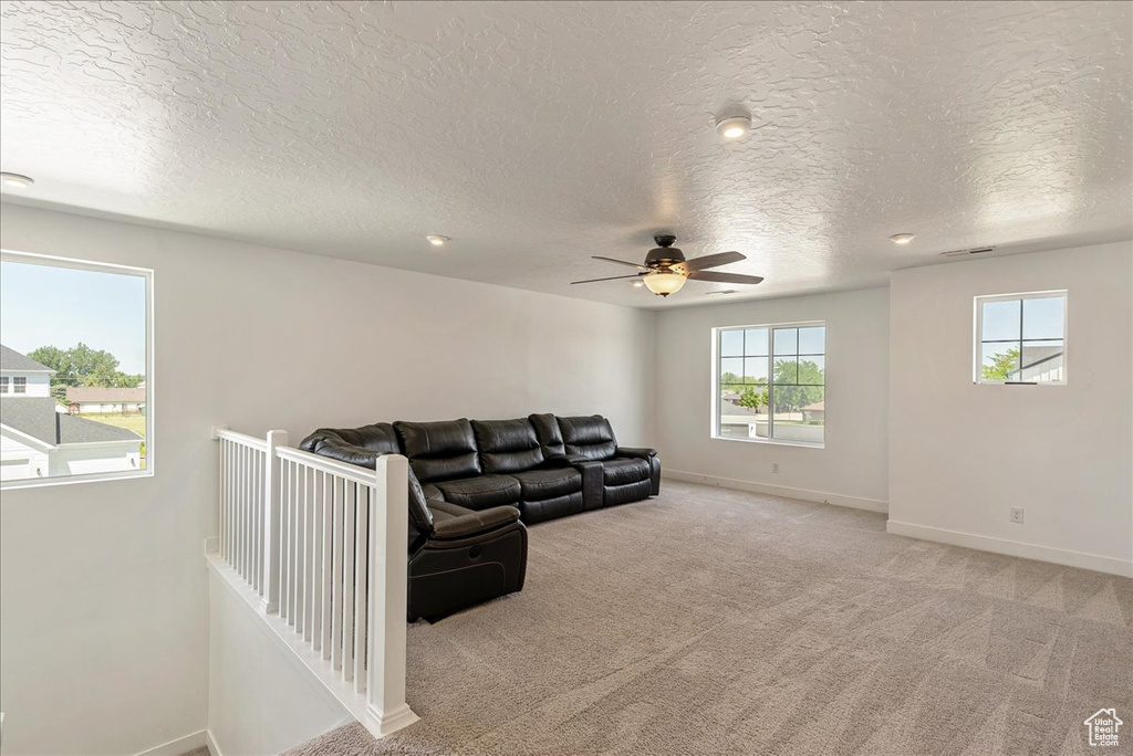 Carpeted living room with ceiling fan, baseboards, and a textured ceiling