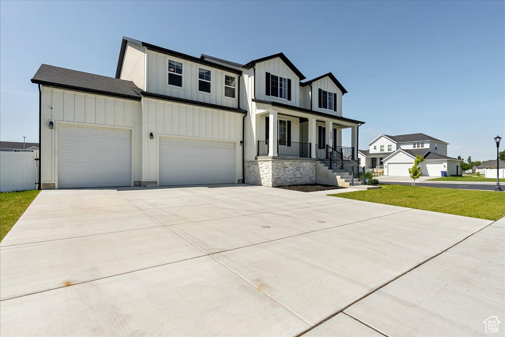 Modern farmhouse with covered porch, board and batten siding, concrete driveway, an attached garage, and a residential view
