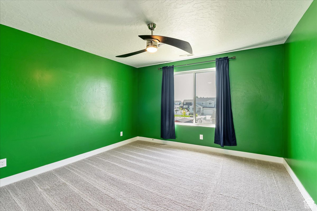 Spare room featuring a textured ceiling, ceiling fan, baseboards, and carpet