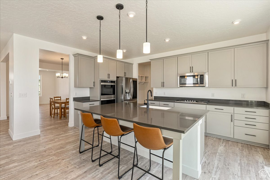Kitchen with stainless steel appliances, dark countertops, gray cabinets, light wood-style flooring, and a textured ceiling