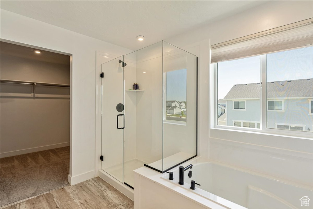 Bathroom with a stall shower, a spacious closet, a garden tub, wood finished floors, and baseboards