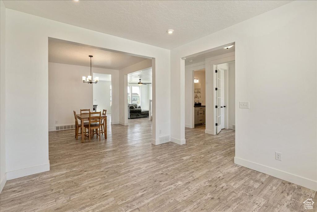 Spare room featuring light wood-style floors, baseboards, a chandelier, ceiling fan, and a textured ceiling