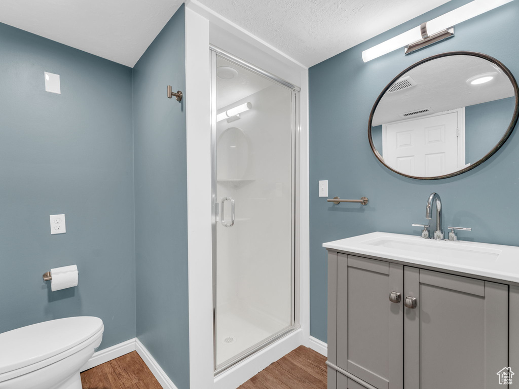Full bathroom featuring baseboards, wood finished floors, a shower stall, vanity, and toilet