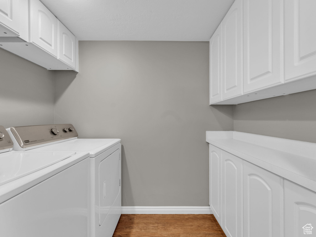 Washroom with washing machine and dryer, cabinet space, baseboards, and wood finished floors