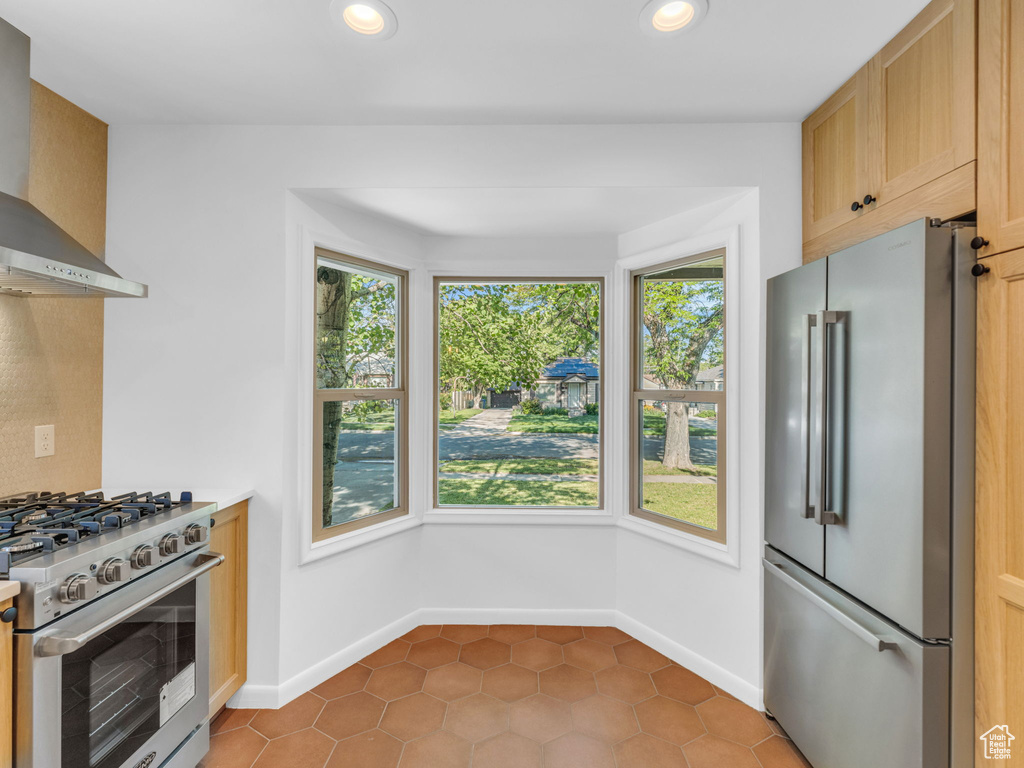 Kitchen with high end appliances, wall chimney range hood, healthy amount of natural light, tile patterned floors, and recessed lighting