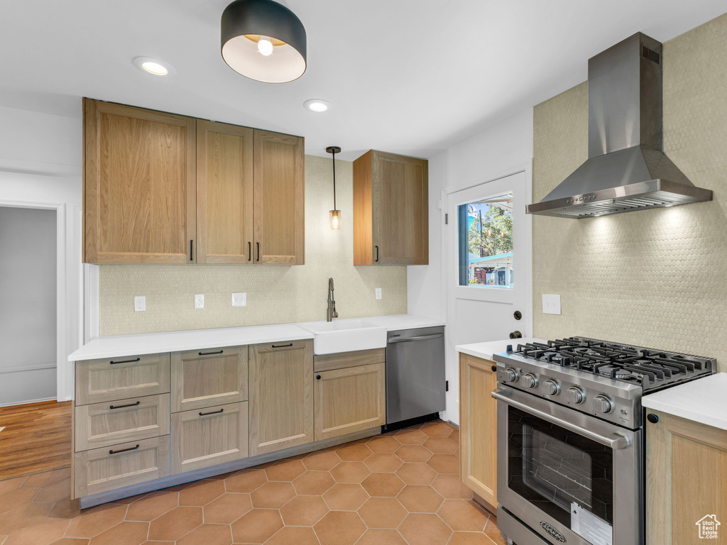 Kitchen with wall chimney exhaust hood, stainless steel appliances, backsplash, a sink, and light countertops