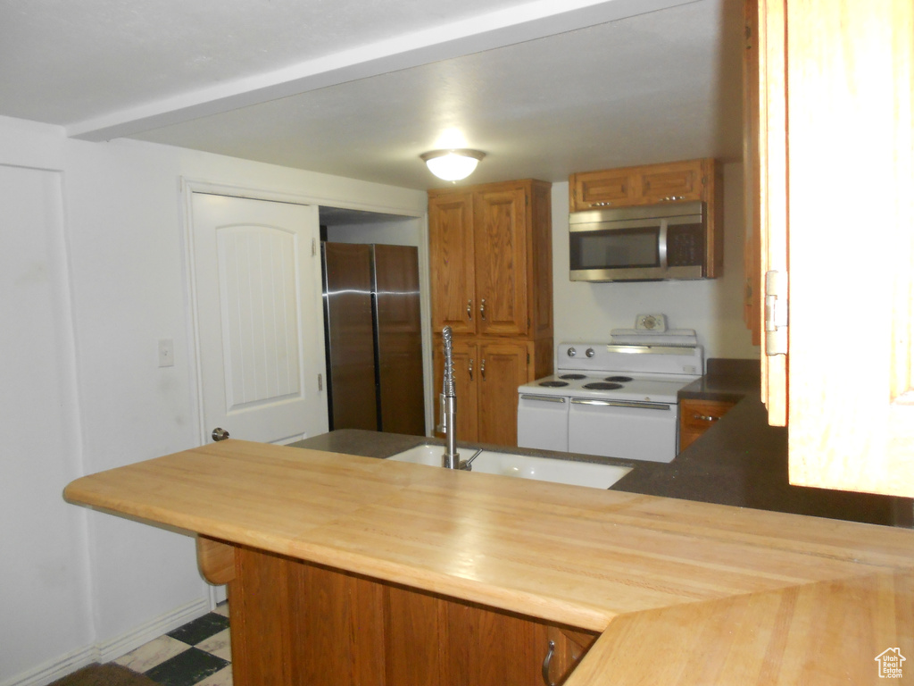 Kitchen featuring stainless steel microwave, refrigerator, white electric stove, a sink, and brown cabinetry