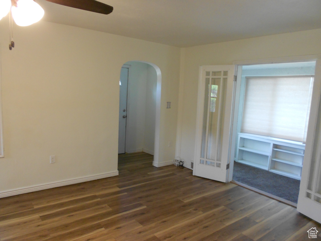 Empty room featuring arched walkways, wood finished floors, ceiling fan, french doors, and baseboards