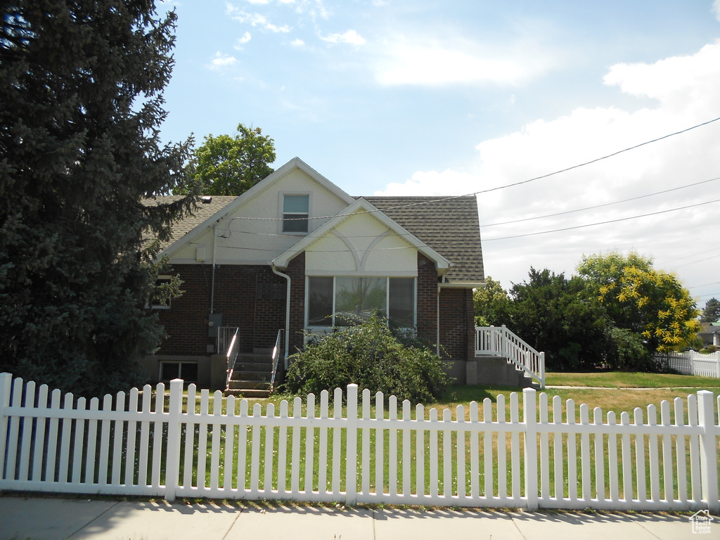 View of front of property with a shingled roof, brick siding, a fenced front yard, and stairway