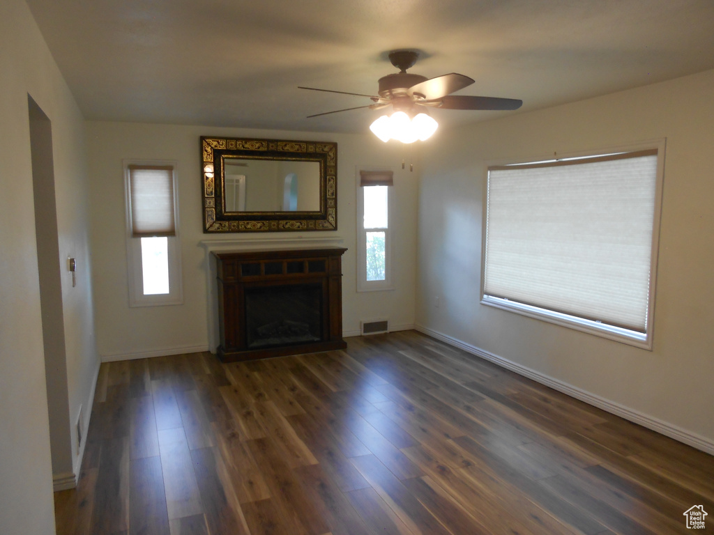Unfurnished living room featuring healthy amount of natural light, ceiling fan, wood finished floors, and a fireplace