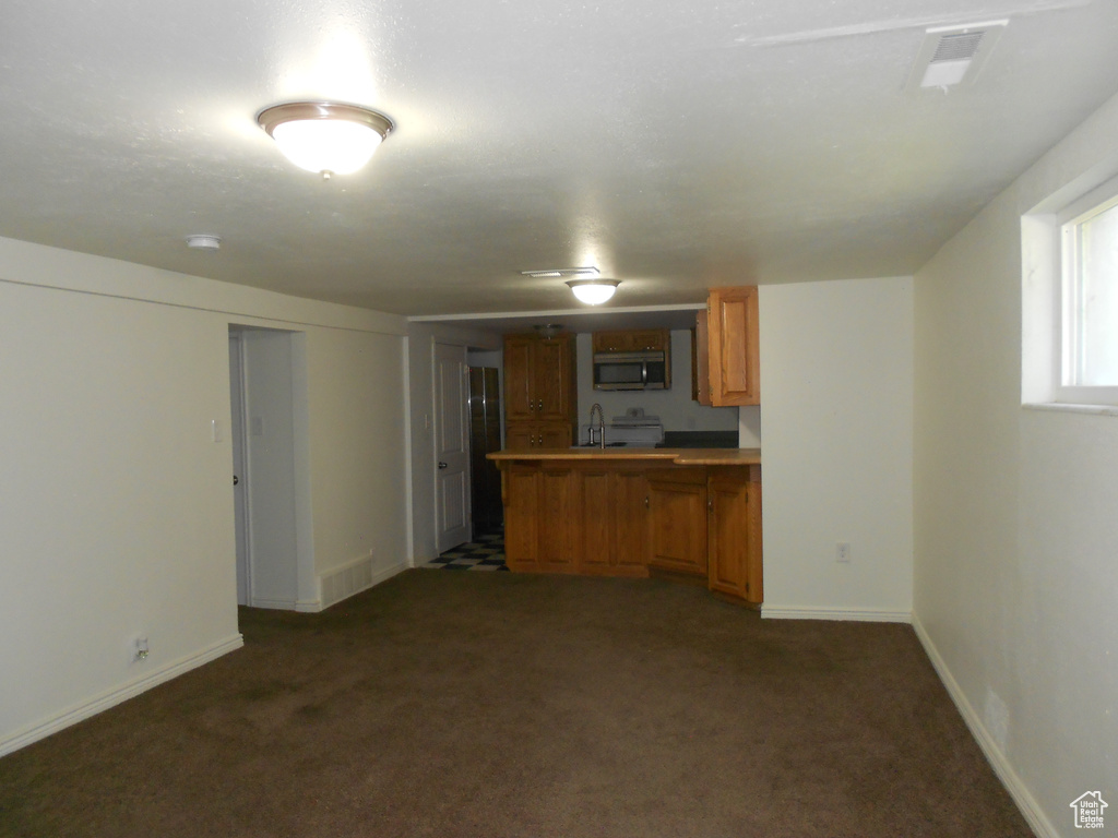 Kitchen with stainless steel microwave, brown cabinetry, a peninsula, a sink, and dark carpet