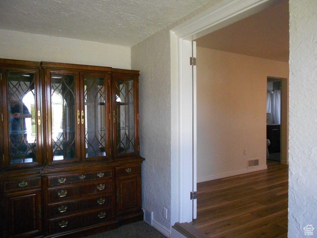Hallway with a textured wall, dark wood-type flooring, baseboards, and a textured ceiling