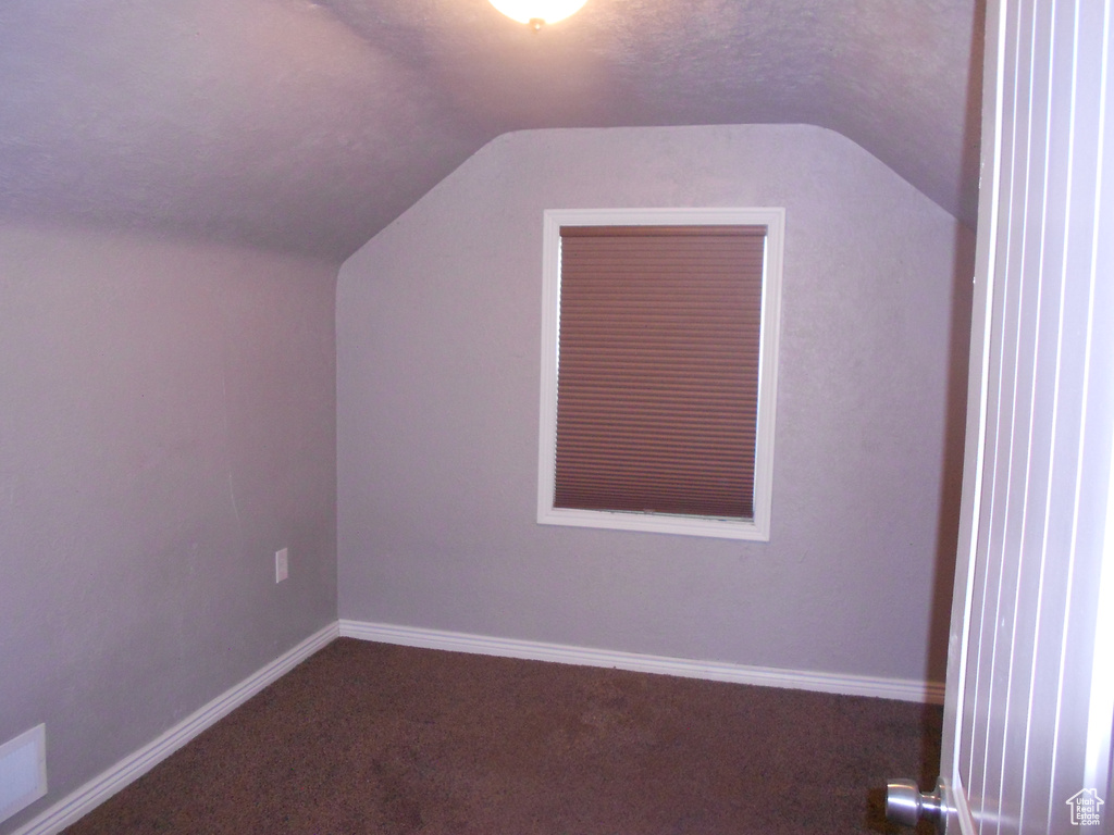 Bonus room featuring vaulted ceiling, dark carpet, and baseboards
