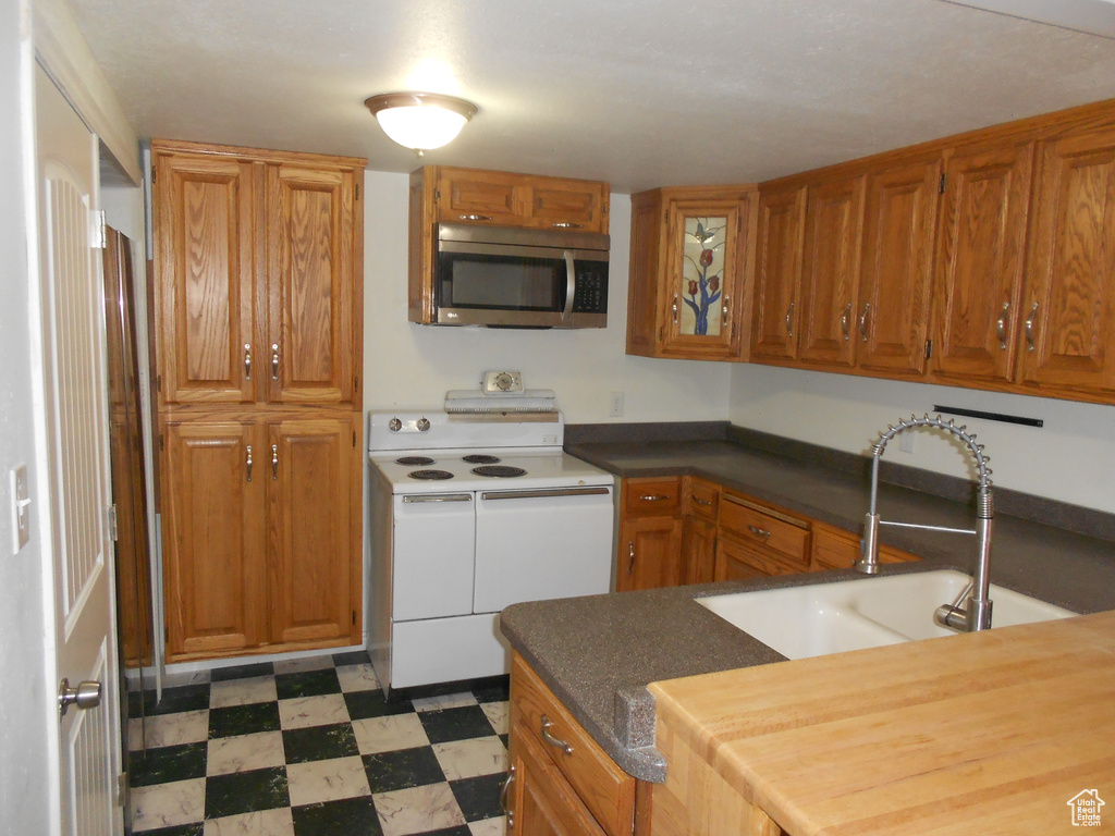 Kitchen with stainless steel microwave, white range with electric cooktop, a sink, tile patterned floors, and brown cabinets
