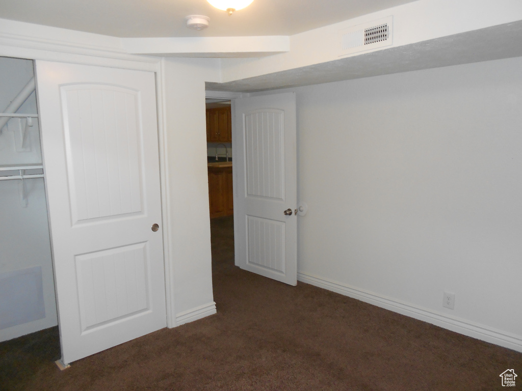 Unfurnished bedroom with dark colored carpet, a closet, and baseboards