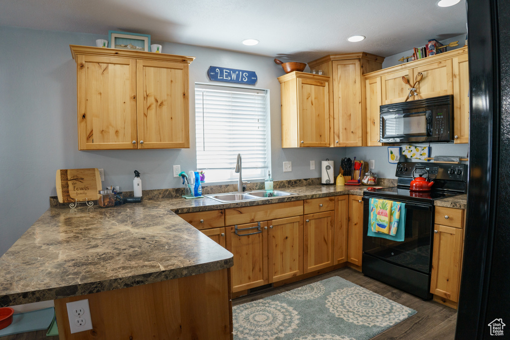 Kitchen with black appliances, a sink, a peninsula, dark countertops, and dark wood-type flooring