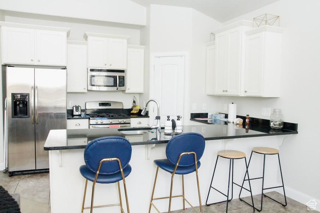 Kitchen featuring appliances with stainless steel finishes, a sink, dark countertops, and white cabinetry