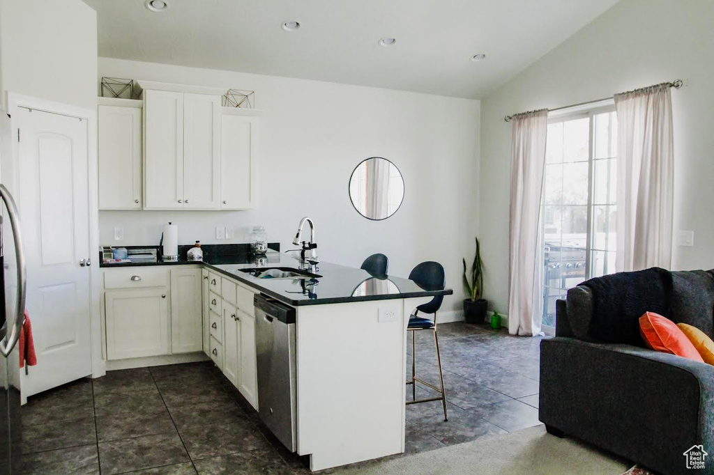 Kitchen with a sink, dark countertops, stainless steel dishwasher, a breakfast bar area, and a peninsula