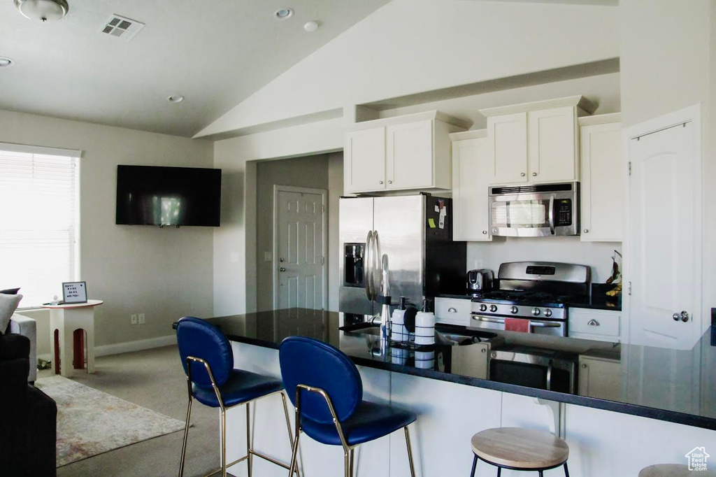 Kitchen featuring appliances with stainless steel finishes, a kitchen bar, dark countertops, white cabinets, and baseboards