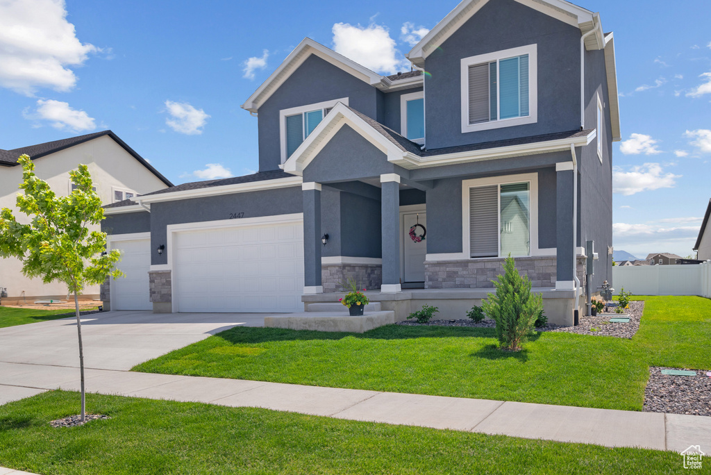 View of front facade with covered porch, stone siding, driveway, stucco siding, and a garage