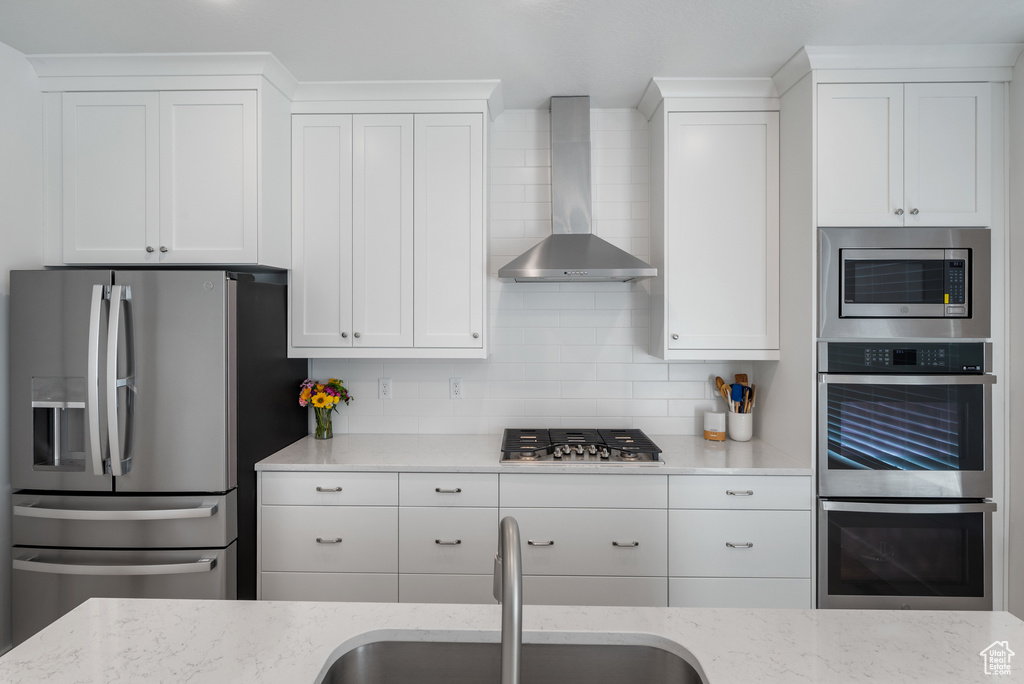 Kitchen featuring stainless steel appliances, wall chimney range hood, a sink, and white cabinetry