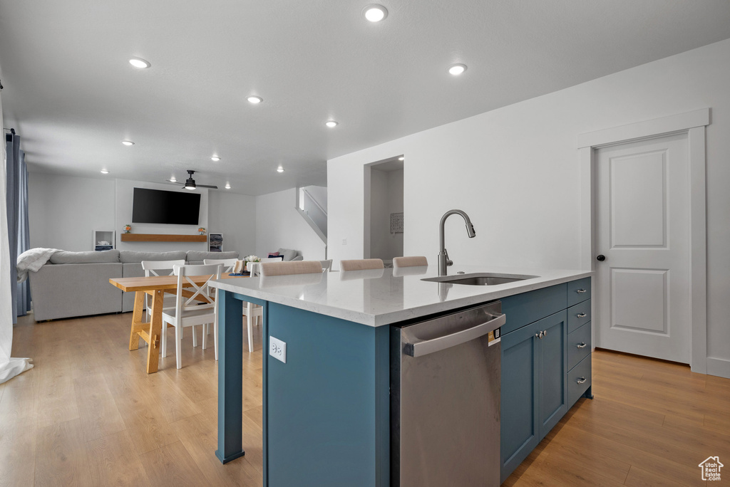 Kitchen featuring dishwasher, a sink, open floor plan, light wood-type flooring, and blue cabinets