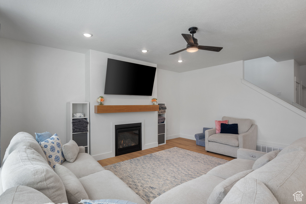 Living area featuring a ceiling fan, wood finished floors, recessed lighting, a glass covered fireplace, and baseboards