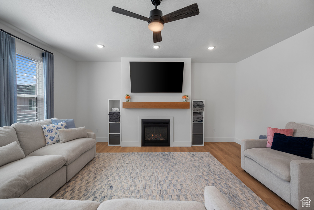 Living room featuring ceiling fan, wood finished floors, baseboards, a lit fireplace, and recessed lighting