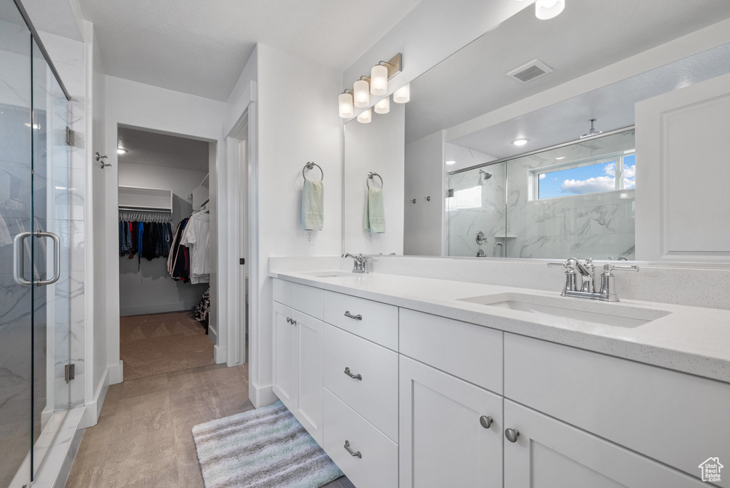 Bathroom featuring a marble finish shower, double vanity, and a walk in closet