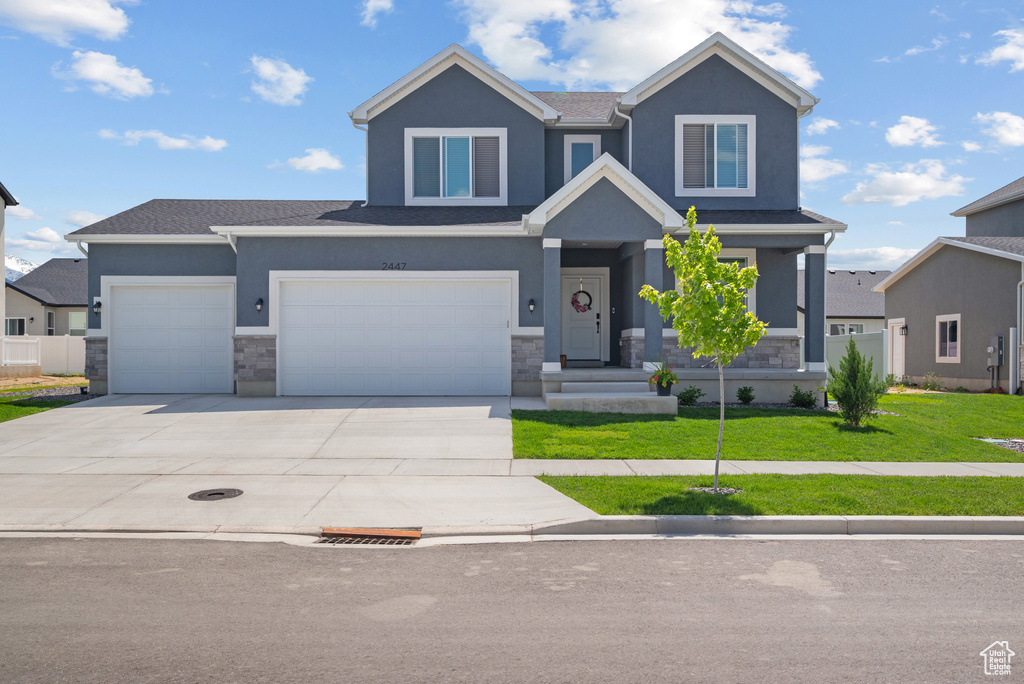 View of front of home with stone siding, a front yard, stucco siding, driveway, and roof with shingles