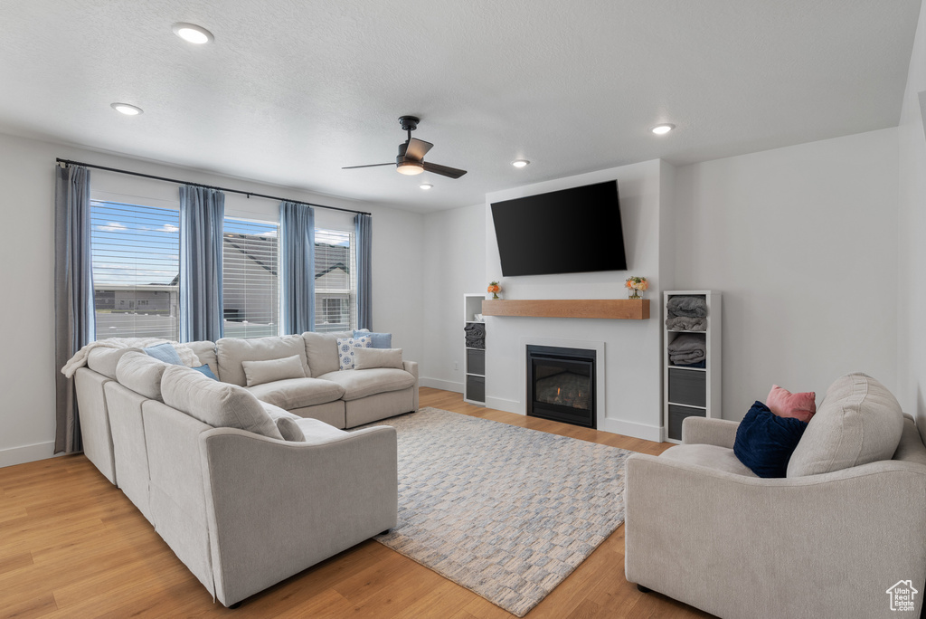 Living area featuring a ceiling fan, light wood-type flooring, a glass covered fireplace, baseboards, and recessed lighting
