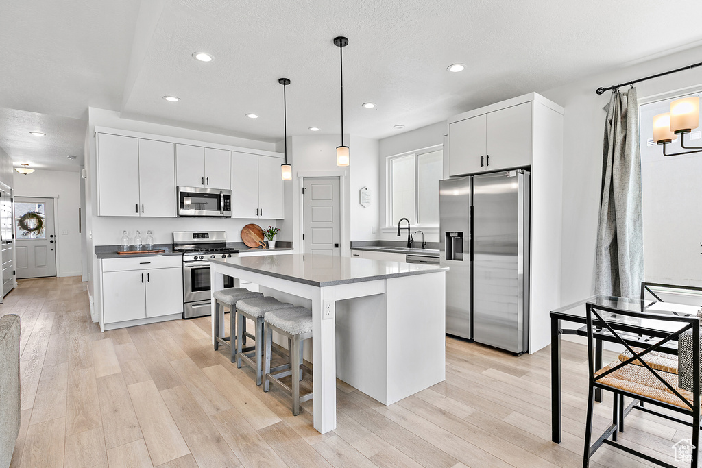 Kitchen with appliances with stainless steel finishes, a kitchen island, dark countertops, light wood finished floors, and recessed lighting