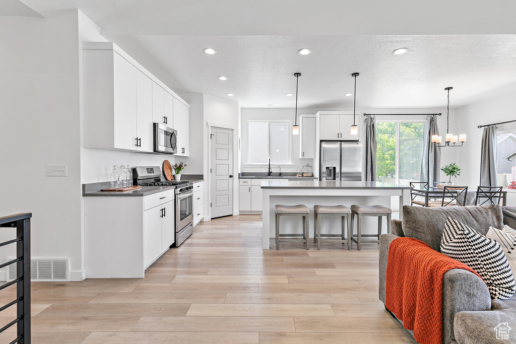 Kitchen featuring appliances with stainless steel finishes, open floor plan, a breakfast bar, light wood-style floors, and dark countertops