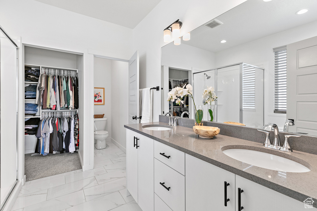 Bathroom with a spacious closet, double vanity, marble finish floors, a stall shower, and toilet