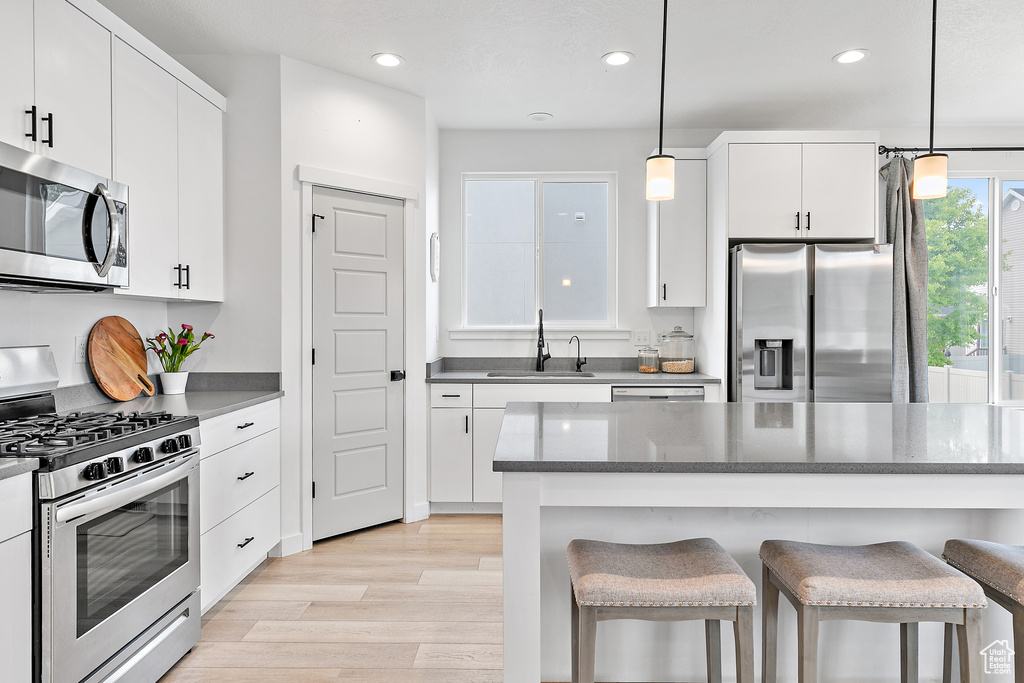 Kitchen with stainless steel appliances, a sink, a kitchen breakfast bar, recessed lighting, and white cabinetry