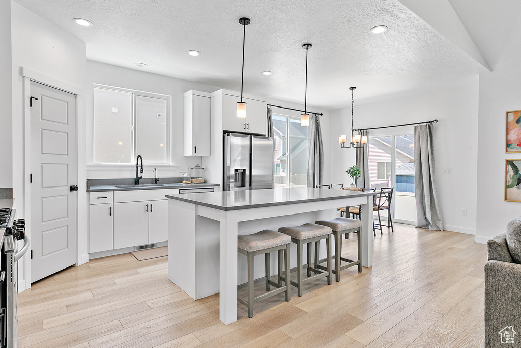 Kitchen featuring stainless steel fridge, a sink, light wood-style flooring, a breakfast bar, and a textured ceiling