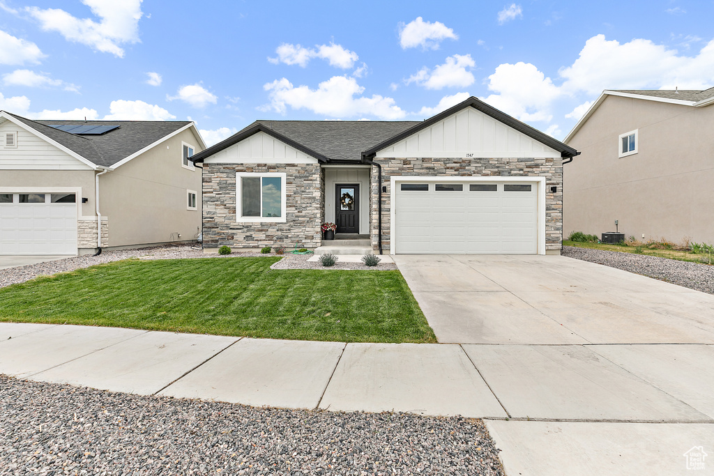 View of front of house with board and batten siding, an attached garage, concrete driveway, a front lawn, and stone siding