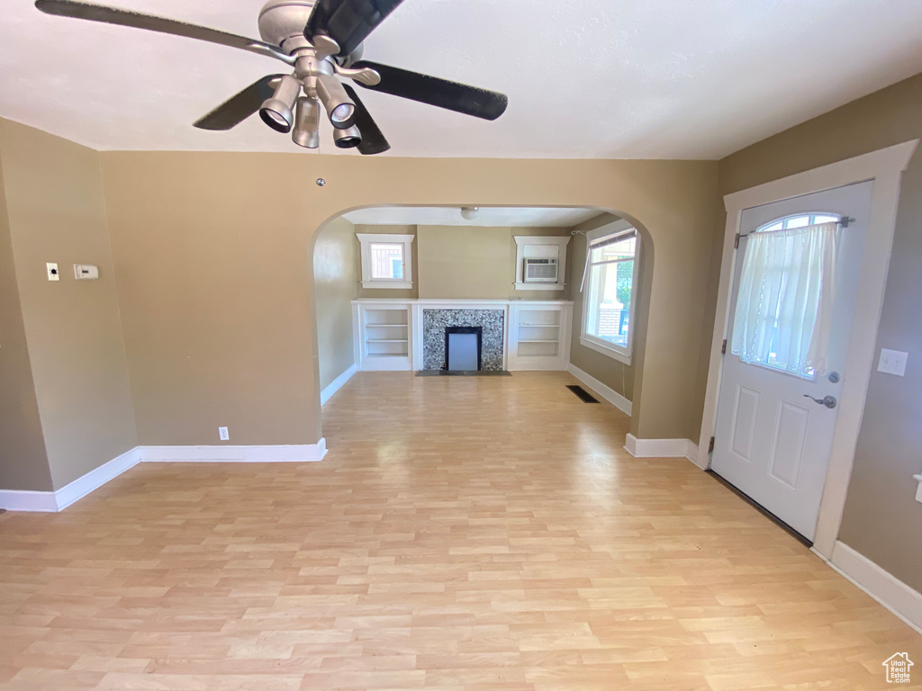 Unfurnished living room featuring arched walkways, light wood-type flooring, baseboards, and ceiling fan