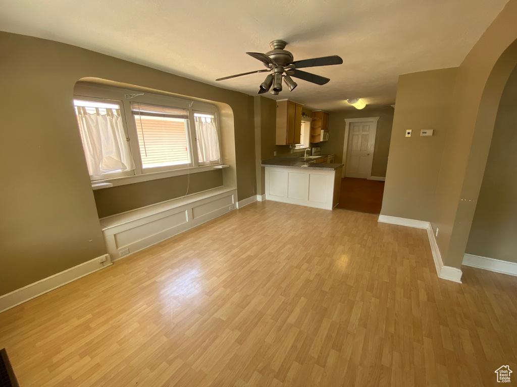 Unfurnished living room with arched walkways, light wood-type flooring, a ceiling fan, baseboards, and a sink