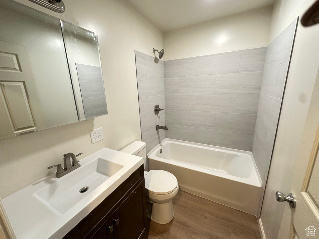 Bathroom with toilet, wood finished floors, vanity, and shower / bath combination
