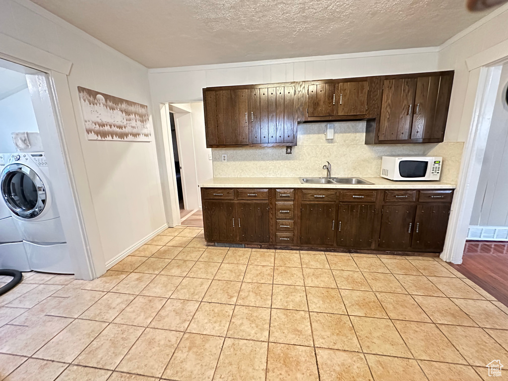 Kitchen with white microwave, a sink, light countertops, decorative backsplash, and dark brown cabinets