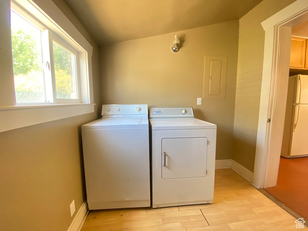 Laundry area featuring electric panel, separate washer and dryer, light wood-style flooring, and baseboards