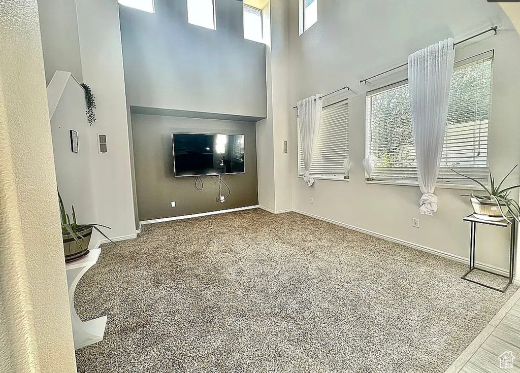 Unfurnished living room featuring a towering ceiling, plenty of natural light, baseboards, and carpet flooring