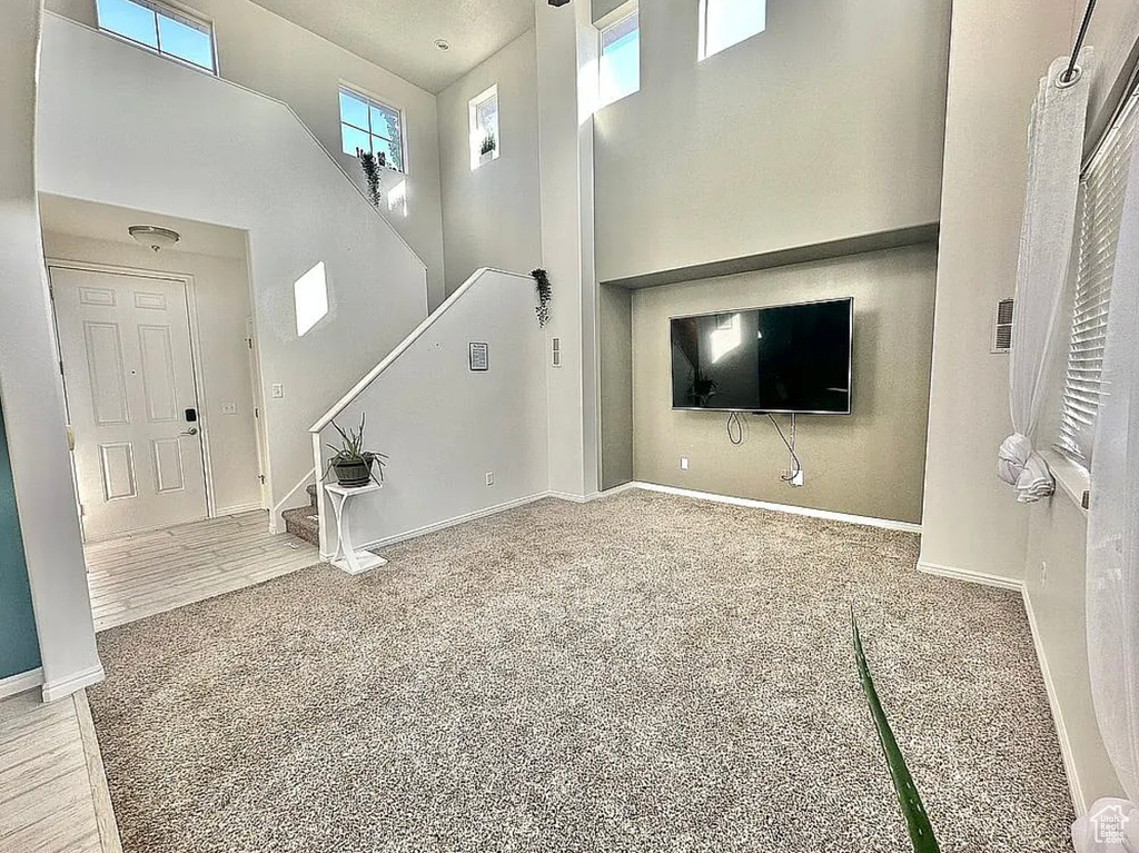 Unfurnished living room featuring a high ceiling, stairway, baseboards, and carpet floors