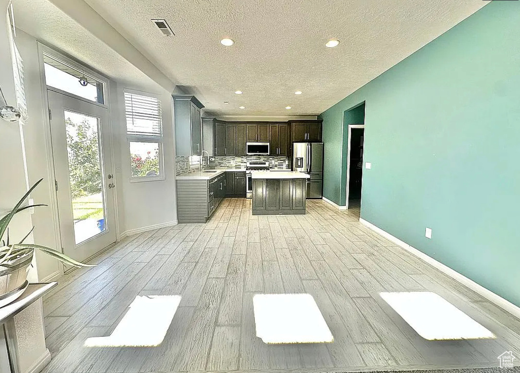 Kitchen featuring appliances with stainless steel finishes, light countertops, light wood-type flooring, a textured ceiling, and decorative backsplash