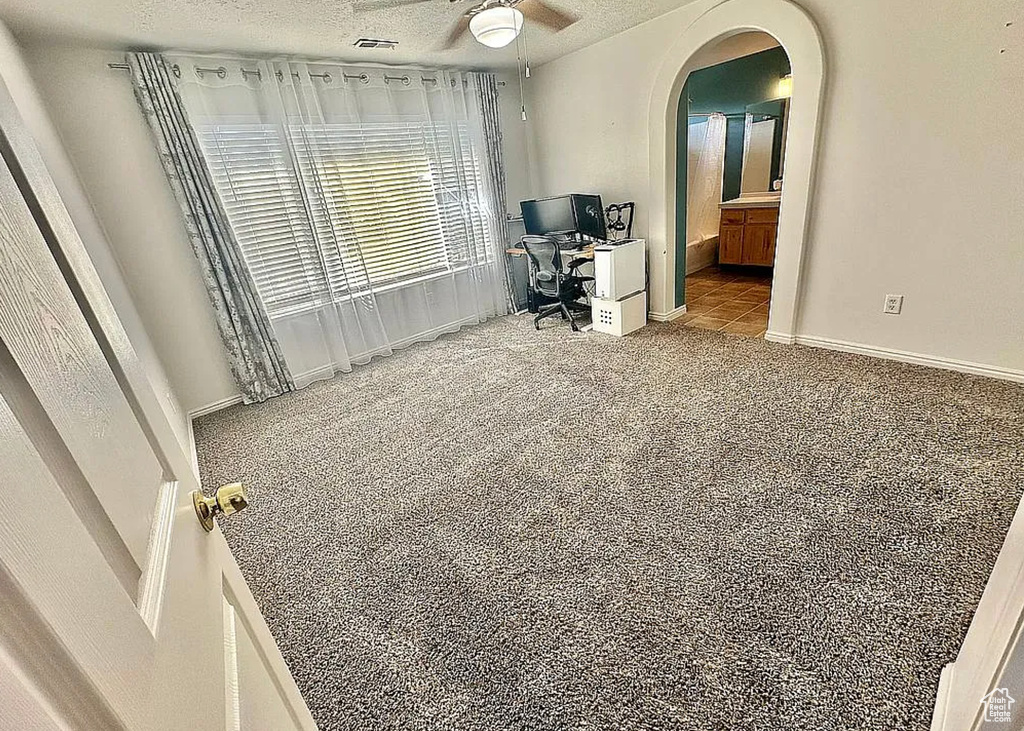Home office featuring ceiling fan, arched walkways, a textured ceiling, and carpet floors