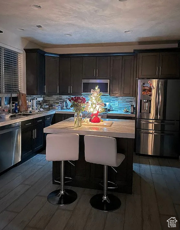 Kitchen with stainless steel appliances, dark wood finished floors, a sink, light countertops, and tasteful backsplash
